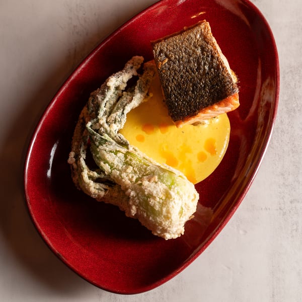 Crispy-skinned salmon with tempura-fried zucchini flower and yellow sauce on a red plate.