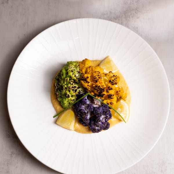 Colorful roasted cauliflower and broccoli florets on a bed of puree, garnished with lemon wedges and chives.