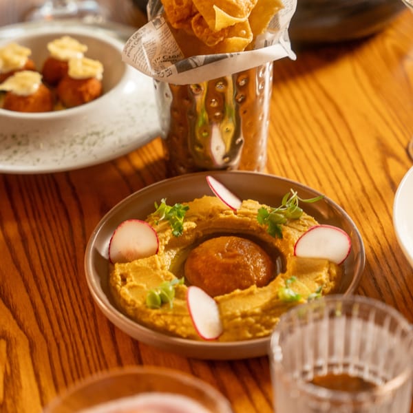 A table spread with hummus, wonton chips in a metal cup, and other appetizers.